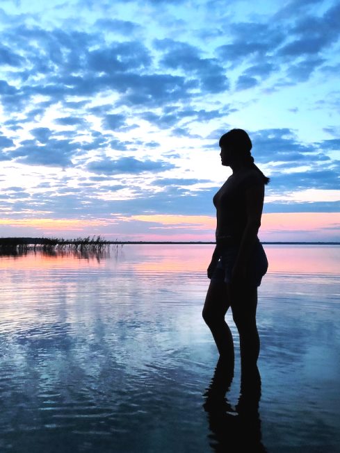 Solitary woman looks out across a quiet still lake.